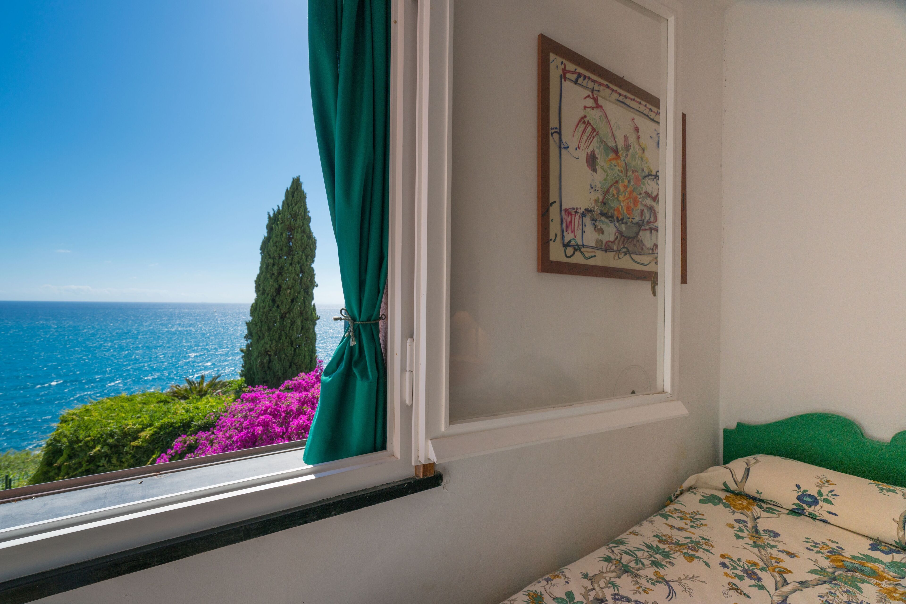 Ein Schlafzimmer mit Meerblick, einem grünen Vorhang und einer blumigen Bettdecke.