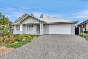 A single-story house with a covered garage, a sloped driveway, and a landscaped front yard. - Tilligerry Beach Retreat (Taylors Beach)