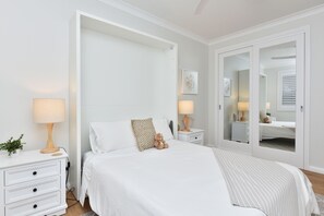 Ein Schlafzimmer mit einem Bett, Nachttischen, einer Kommode, einem Spiegel und einer Topfpflanze.