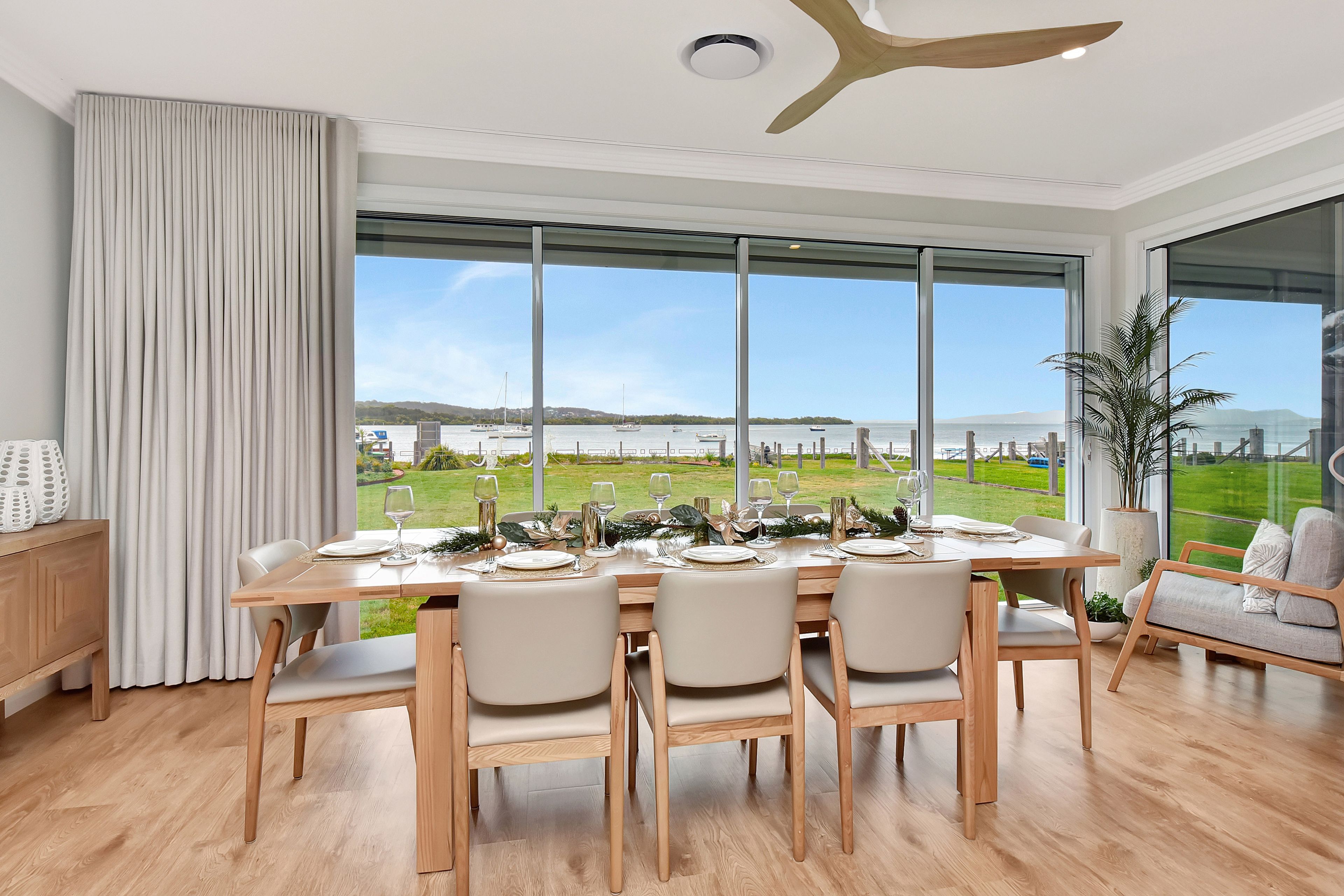 A dining area with a large table set for four, large windows, and a view of the sea.
