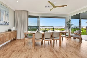 A dining area with a view of a body of water, a ceiling fan, and a dining table set for four. - Tilligerry Beach Retreat (Taylors Beach)