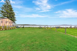 A grassy field with a building and a fence. - Tilligerry Beach Retreat (Taylors Beach)