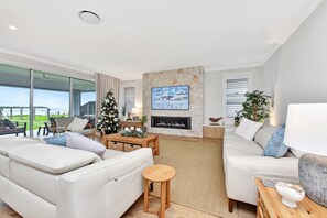 A modern living room with a fireplace, a large window, and a view of the outdoors. - Tilligerry Beach Retreat (Taylors Beach)