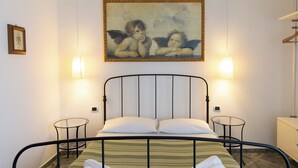 Una cama con estructura metálica, dos mesitas de noche, un cuadro colgado en la pared y una lámpara colgante.