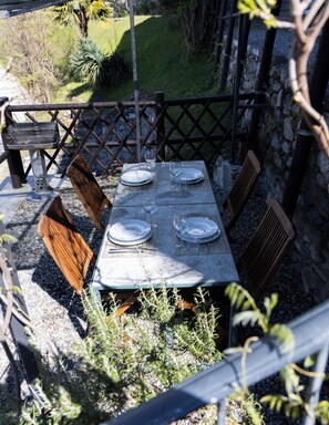 Un área de comedor al aire libre con una mesa dispuesta para cuatro personas, rodeada de sillas de madera y una parrilla de metal.