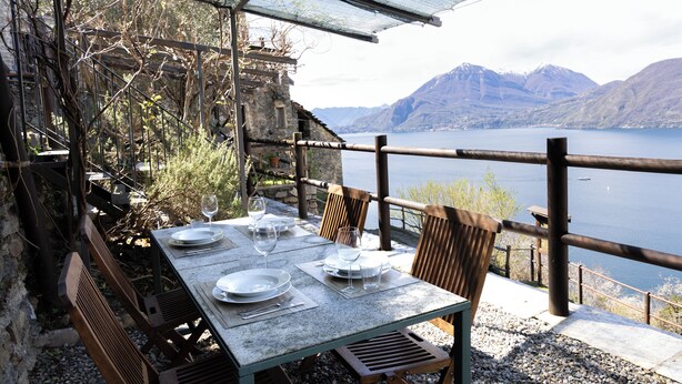 Un espacio de comedor al aire libre con una mesa preparada para cuatro personas, con vista a un lago y montañas.