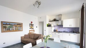 Una cocina moderna con armarios blancos, un microondas y una estufa a gas. Hay un comedor con una mesa y sillas, y un cuadro en la pared.