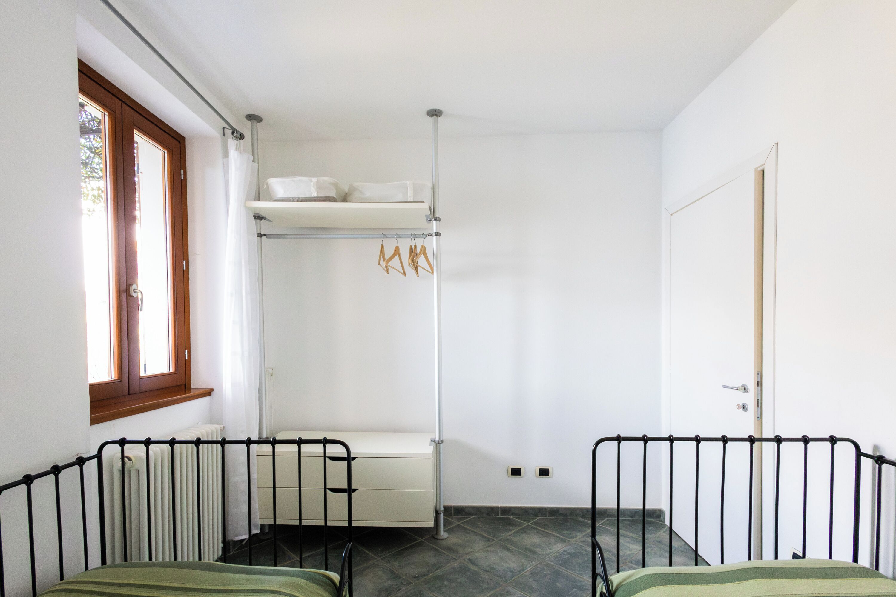 Um quarto com uma cama, um radiador, uma janela e uma porta.
