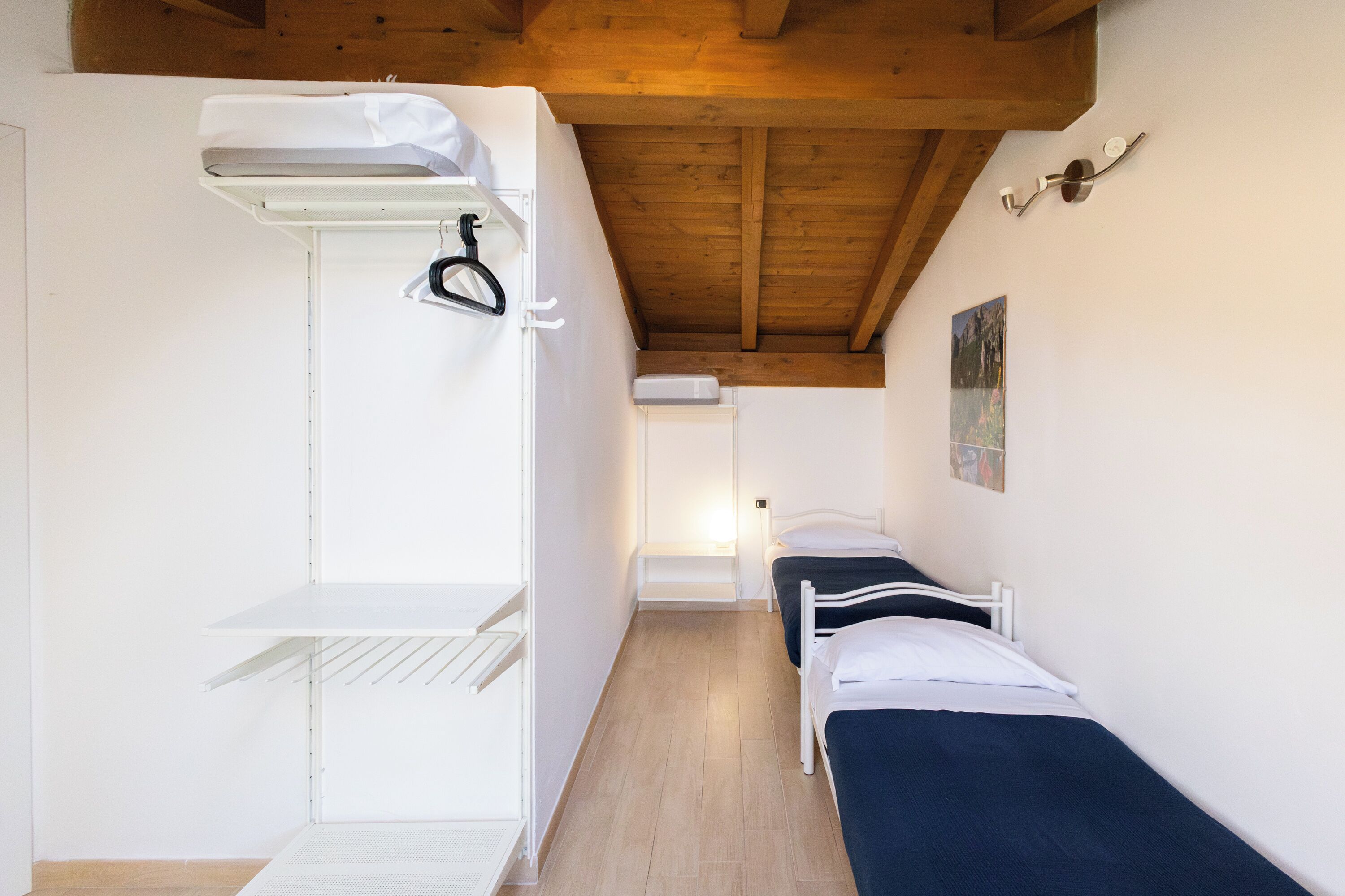 A narrow corridor with two single beds, a white wardrobe, and a wooden ceiling.