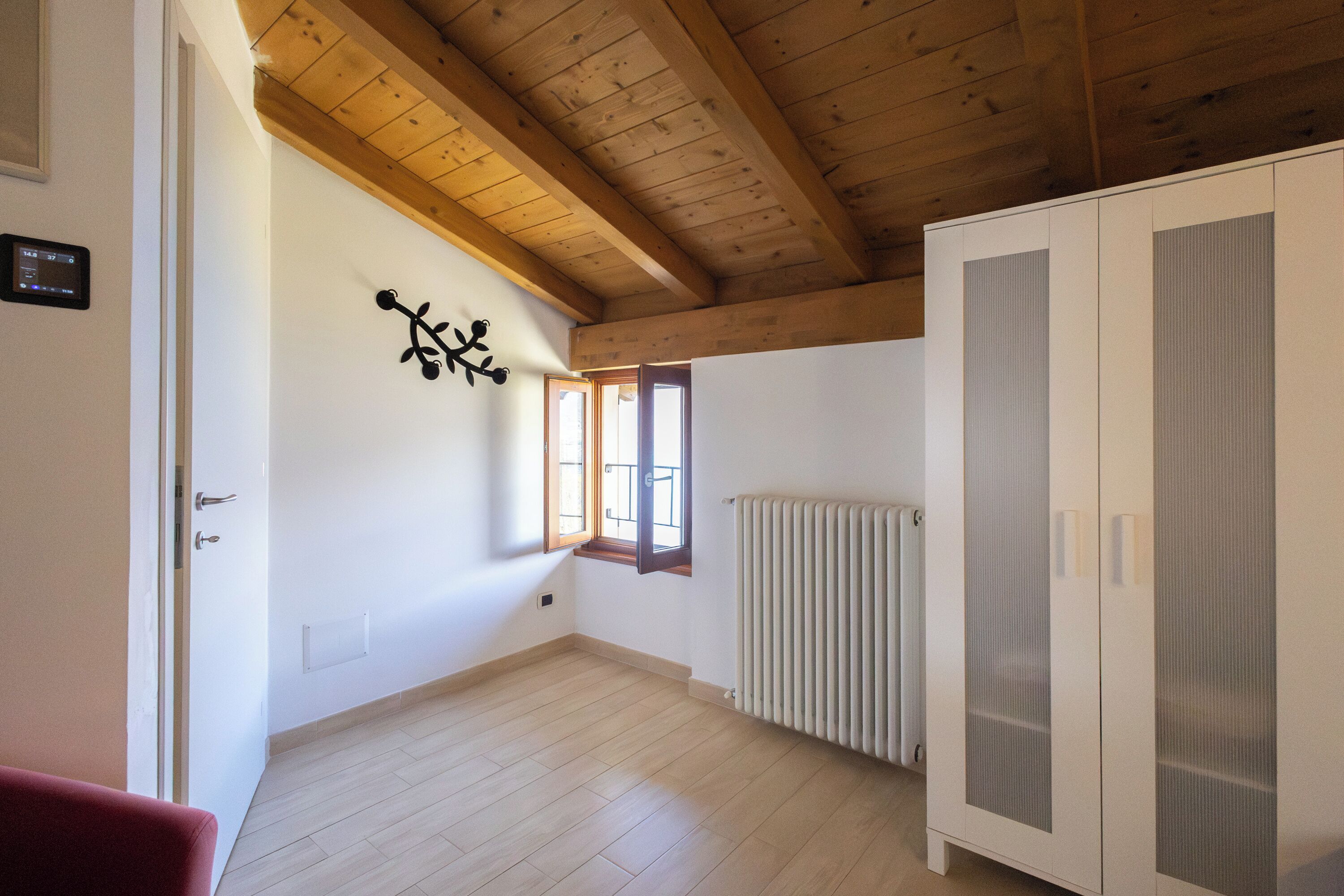 A room with wooden beams, a radiator, a wardrobe, and a window with a view.