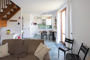 Ein Wohnzimmer mit Sofa, ein Essbereich mit Tisch und Stühlen, eine Küche mit Schränken und einer Mikrowelle sowie eine Treppe.