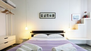 Hotellihuone, jossa on sänky, kaksi rullalle taitettua pyyhettä, seinälle ripustettu taulu ja yöpöytä, jossa on lamppu.