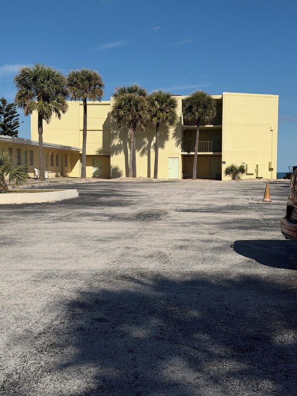A building with a yellow facade, palm trees, and a parking lot. - South Shores Motel (Daytona Beach Shores)