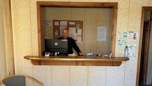 Una reception con scrivania, computer, sedia e bacheca con diversi avvisi.