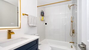 Casa de banho moderna com lavatório branco, acessórios dourados, sanita branca e banheira com chuveiro.