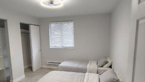 Quarto com cama, janela com persianas, luminária no teto e porta para um armário.