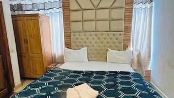 Une chambre à coucher avec un lit, une armoire en bois, une tête de lit capitonnée et une couvre-lit à motifs.