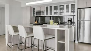 Une cuisine moderne avec des meubles blancs, des appareils en acier inoxydable et un îlot central doté de tabourets de bar.