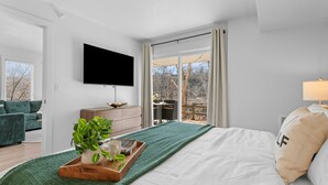 Un dormitorio moderno con una cama grande, un televisor montado en la pared y vistas al exterior a través de un ventanal corredero.