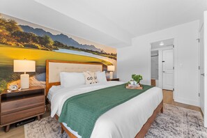A bedroom with a large bed, a nightstand with a lamp, a wall mural, and a door to another room. - Roark Creek Resort (Branson)