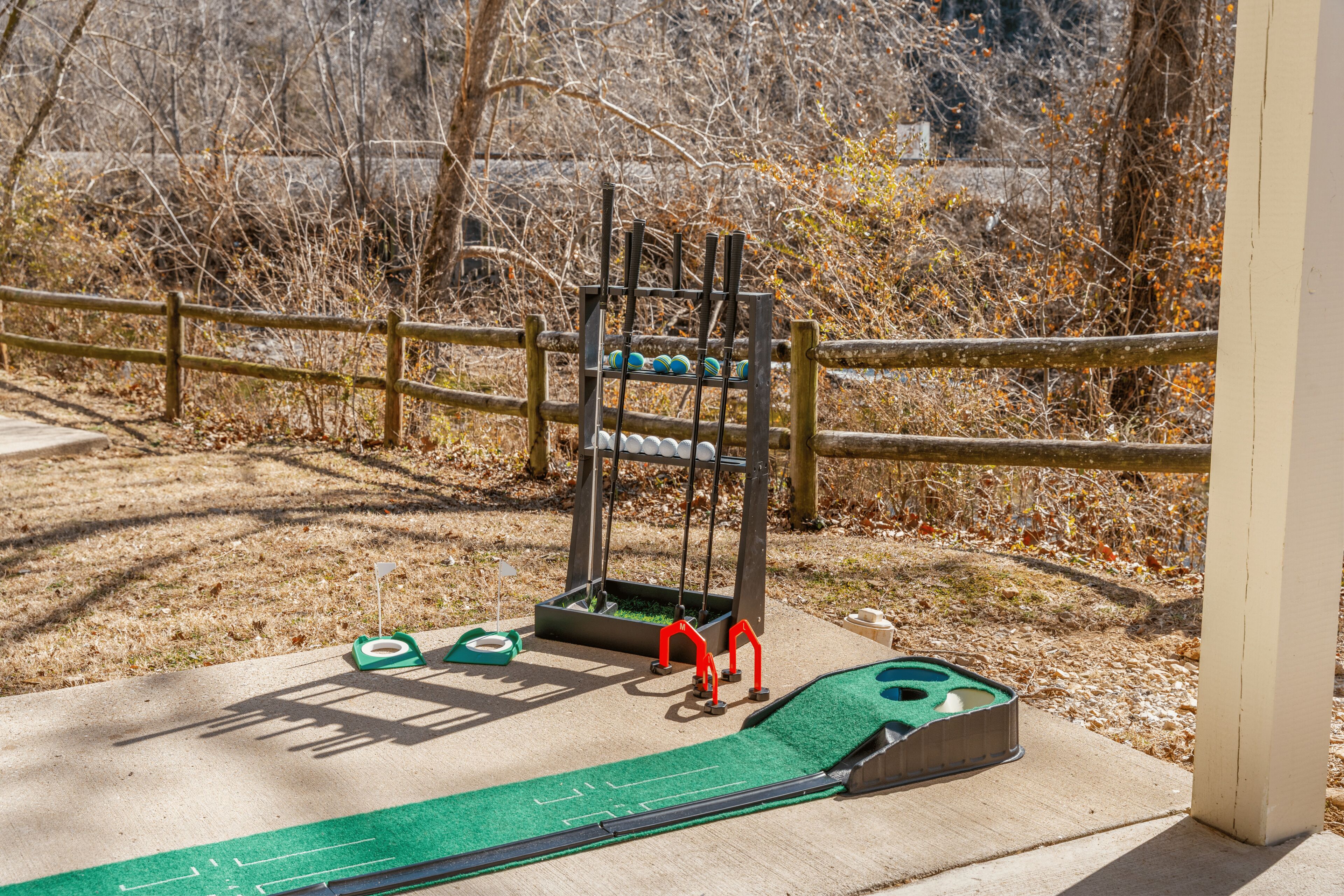 A miniature golf course with a green putting mat, a red golf hole, and a wooden fence.