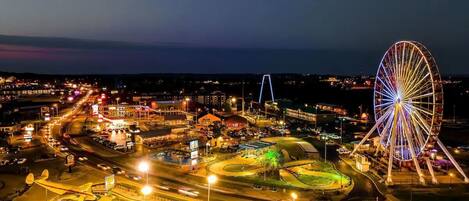 A large Ferris wheel with colorful lights, surrounded by a well-lit amusement park area with various rides and attractions.
