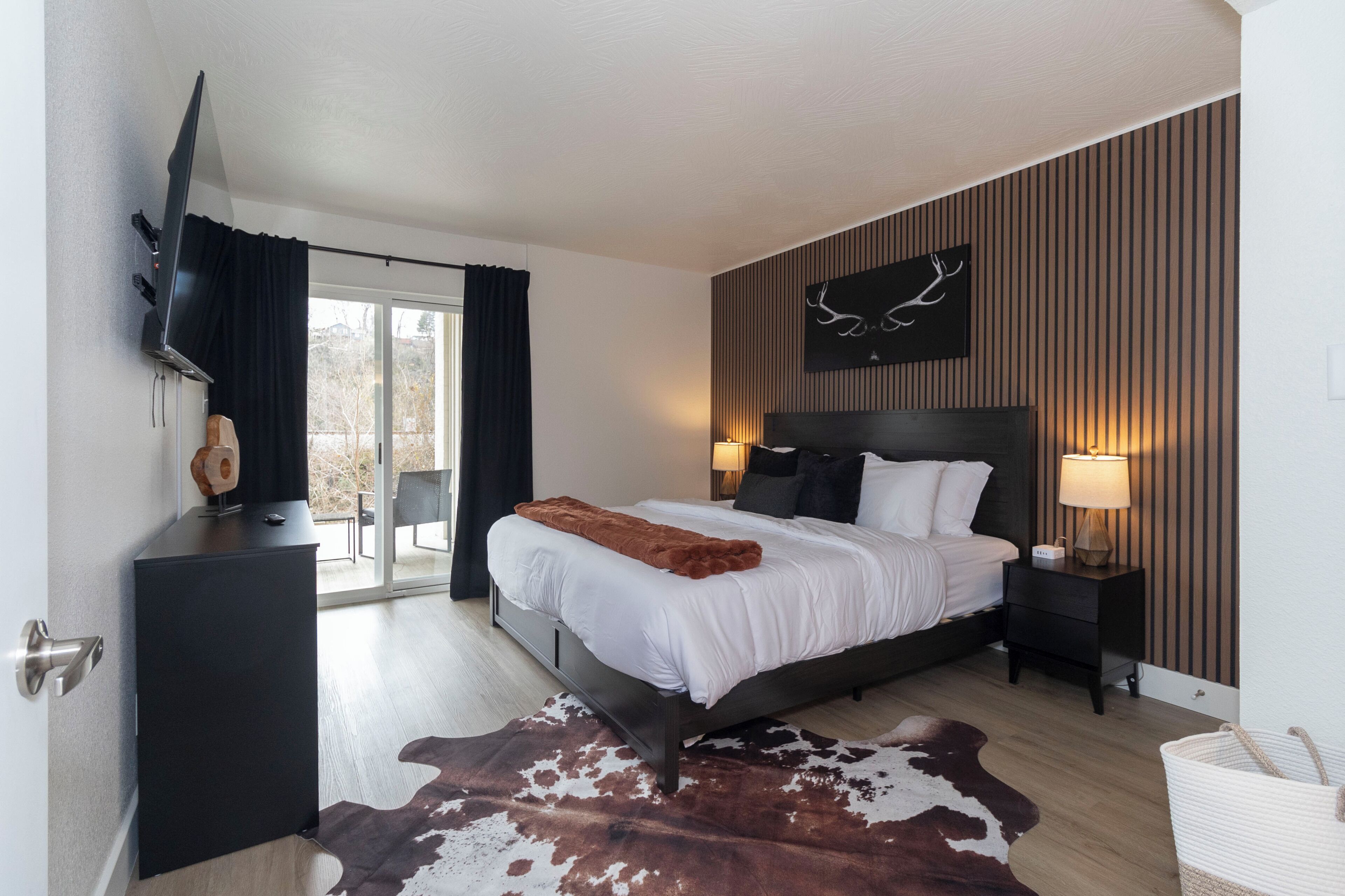 Ein modernes Hotelzimmer mit einem großen Bett, einem flachbildfernseher an der Wand, einem Holzkopfstück und einem Kuhfellteppich.