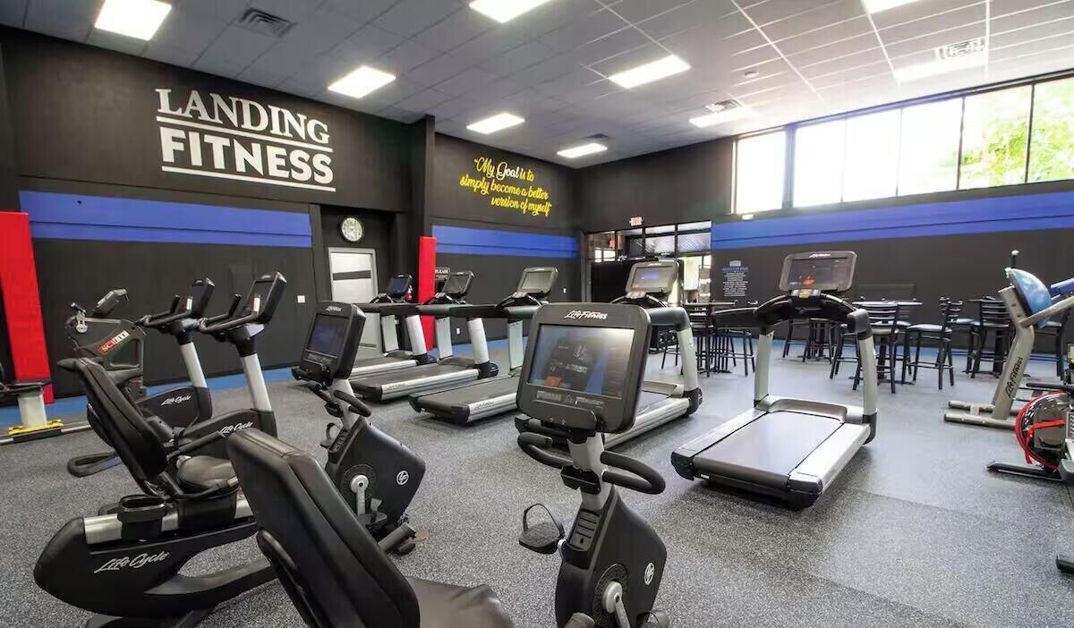 A gym with multiple treadmills and elliptical machines, a motivational quote on the wall, and a large window providing natural light.