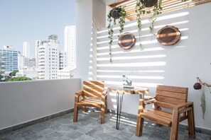Ein Balkon mit zwei Holzstühlen, einem kleinen Tisch und hängenden Pflanzen.