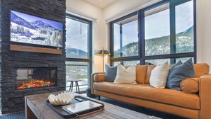 A living room with a stone fireplace, a leather sofa, and large windows with a mountain view.