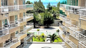 Ein mehrstöckiges Gebäude mit Balkonen, einem zentralen Innenhof mit einem kreisförmigen Wasserspiel und Blick auf das Meer.