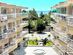 Um edifício com vários andares e varandas, um pátio central com um espelho d'água circular e vista para o mar.