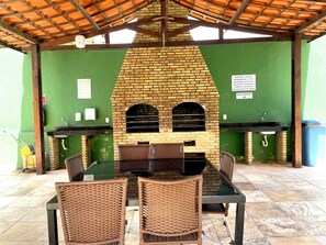 An outdoor patio with a brick oven, two sinks, wicker chairs, and a table. - BP03 - Varanda Ventilada No Estilo Bali Lounge (Caucaia)