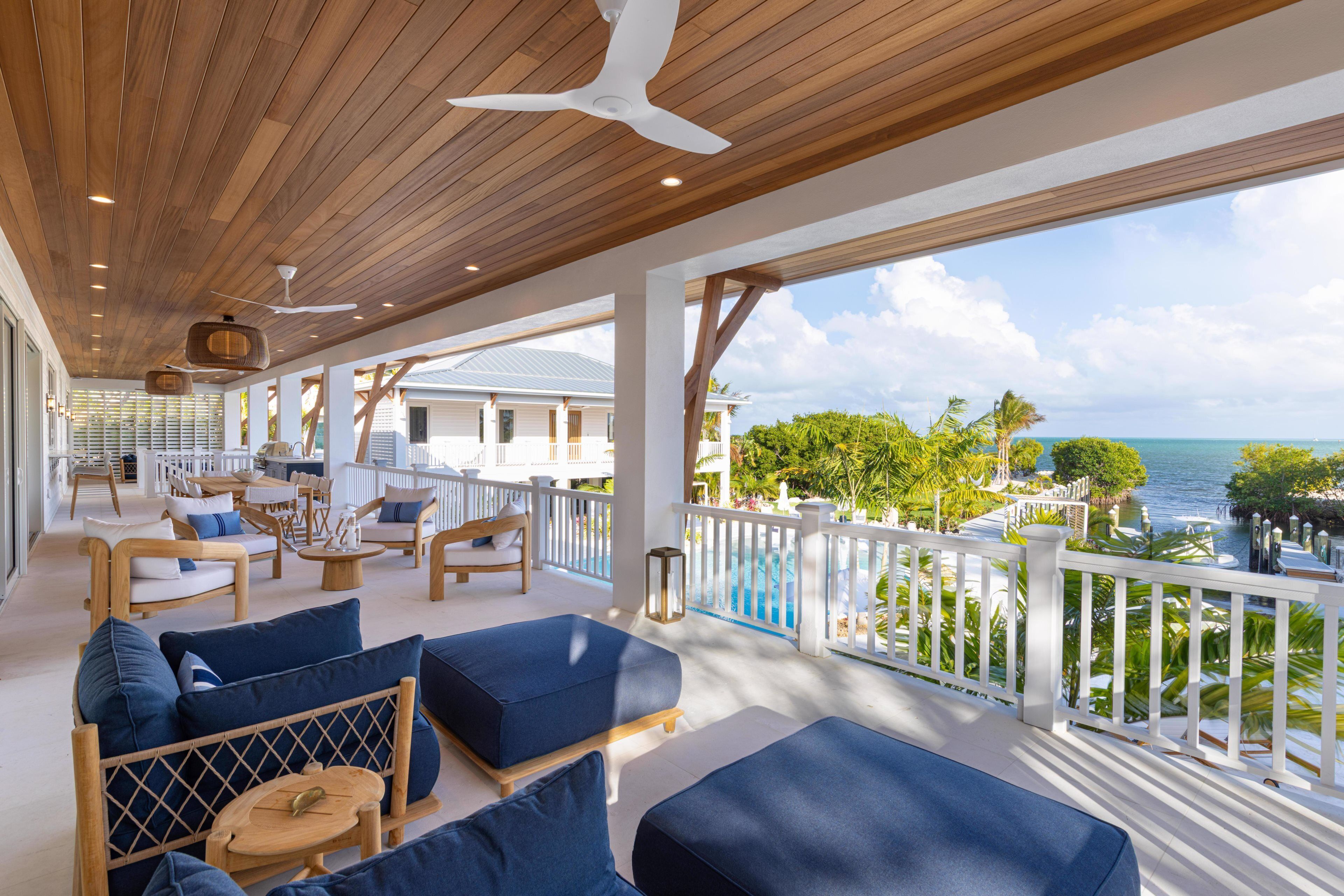 A covered outdoor area with wooden flooring, blue cushioned seating, a white railing, and a view of the ocean.