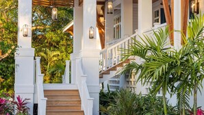 A modern house with a covered porch, wooden stairs, and a garden with tropical plants.