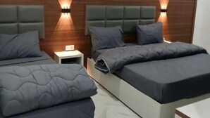 Quarto moderno com duas camas, uma mesa de cabeceira e iluminação embutida na parede.
