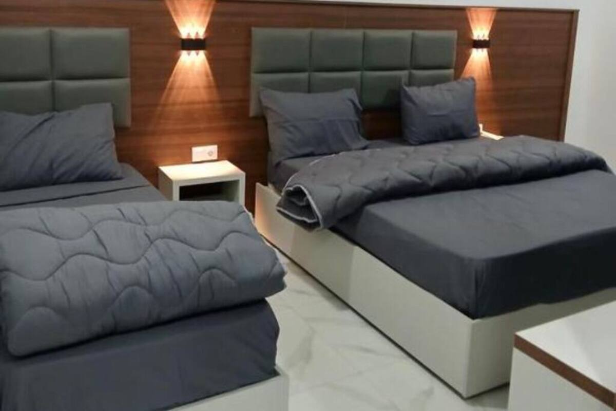 A modern bedroom with two beds, a nightstand, and wall-mounted lighting.