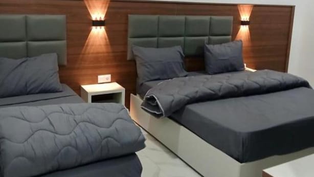 Quarto de hotel moderno com duas camas, cada uma com cabeceira e abajures.
