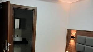 Quarto com cama, mesa de cabeceira, luminária na parede e porta para o banheiro.