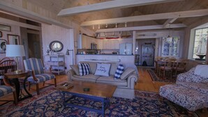 Amplia sala de estar con sofá, sillas y una mesa de centro. Se observa una zona de cocina al fondo.