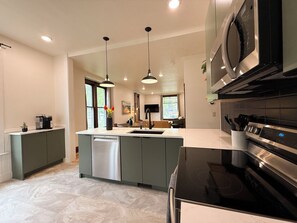 Una cocina moderna con una isla central, electrodomésticos de acero inoxidable e iluminación colgante.