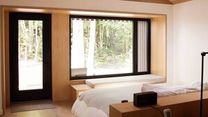 Een moderne slaapkamer met een groot bed, een bureau en uitzicht op een bos door de ramen.