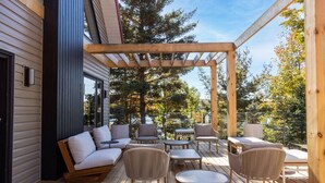 Een houten terras met buitenmeubilair, waaronder een bank en stoelen, onder een pergola.