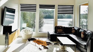 Un salon moderne doté d’une grande fenêtre, d’un canapé en cuir, d’un fauteuil blanc, d’un téléviseur à écran plat et d’un tapis en peau de vache.