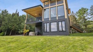 Une maison moderne à deux étages, dotée d’un balcon, de grandes fenêtres et d’une terrasse en bois.