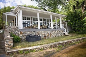 A house with a covered porch, stone foundation, and a small outdoor seating area.
