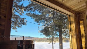 Une cabane en bois dotée d’une grande fenêtre donnant sur un paysage enneigé et des arbres.
