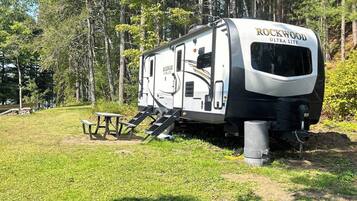 Un camping-car Rockwood Ultra Lite est stationné dans une zone herbeuse, à proximité de quelques tables de pique-nique.