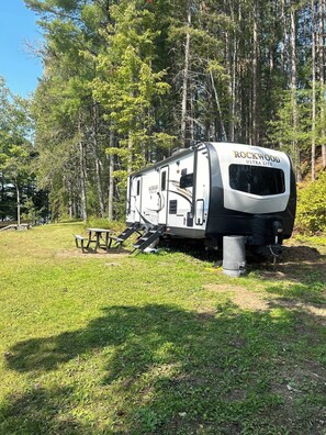 A Rockwood Ultra Lite RV parked in a grassy area with picnic tables nearby.
