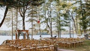 Une cérémonie de mariage en plein air, avec des chaises en bois disposées en rangées, une arche en bois et un mât avec un drapeau.